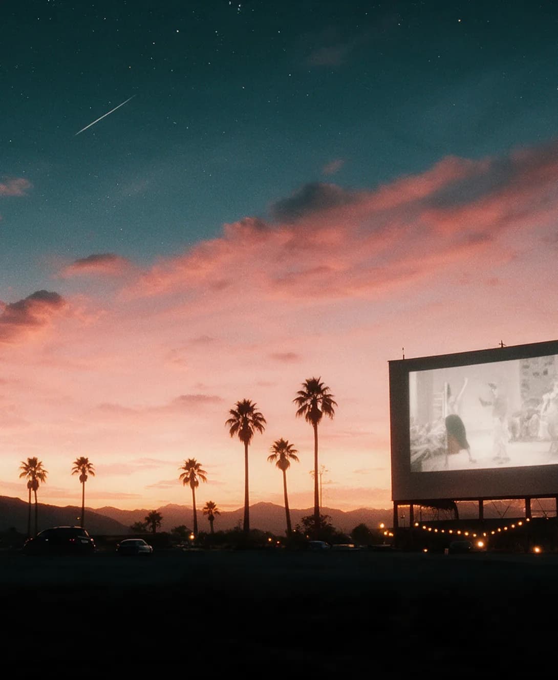 West Wind Drive-In at dusk, with palms and mountains behind the screen